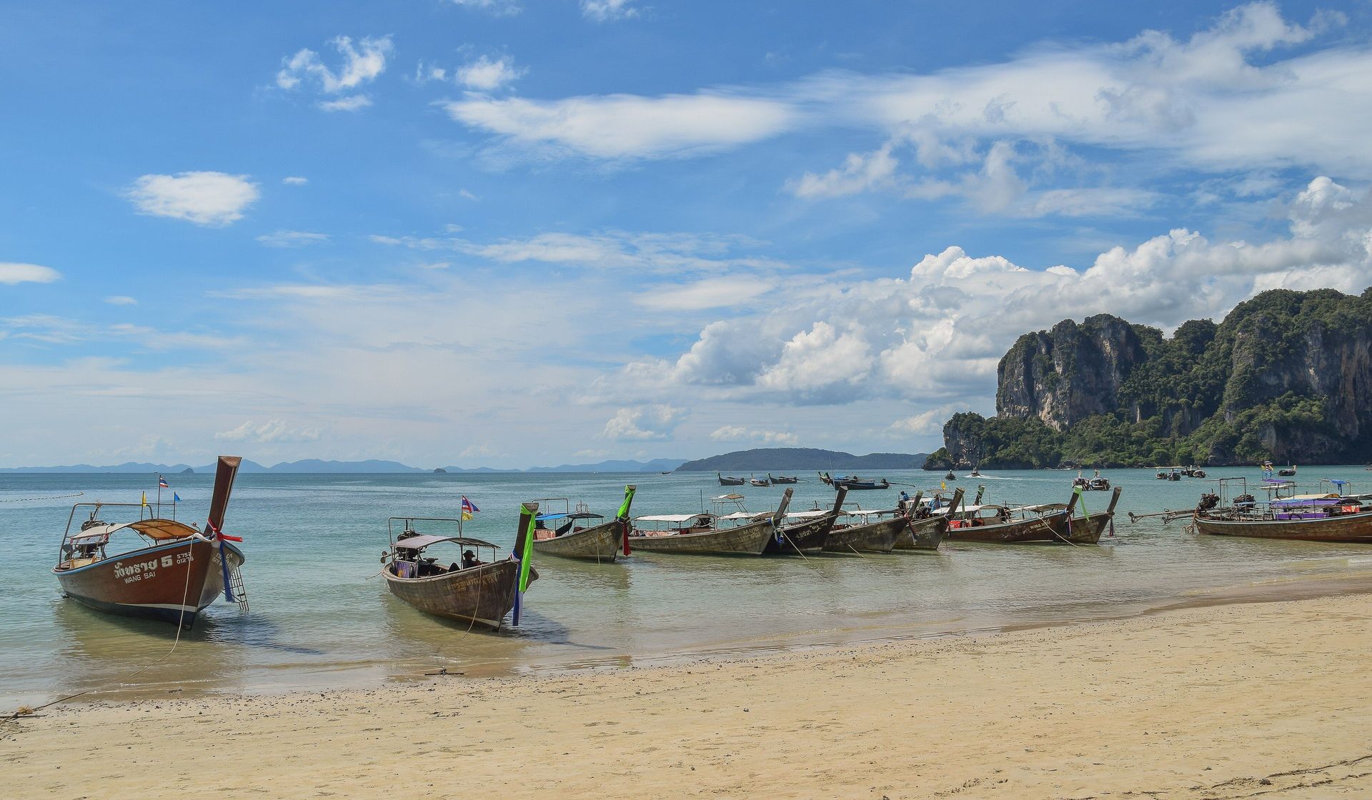 A tropical beach with clear water, distant limestone cliffs, and a quieter shoreline.