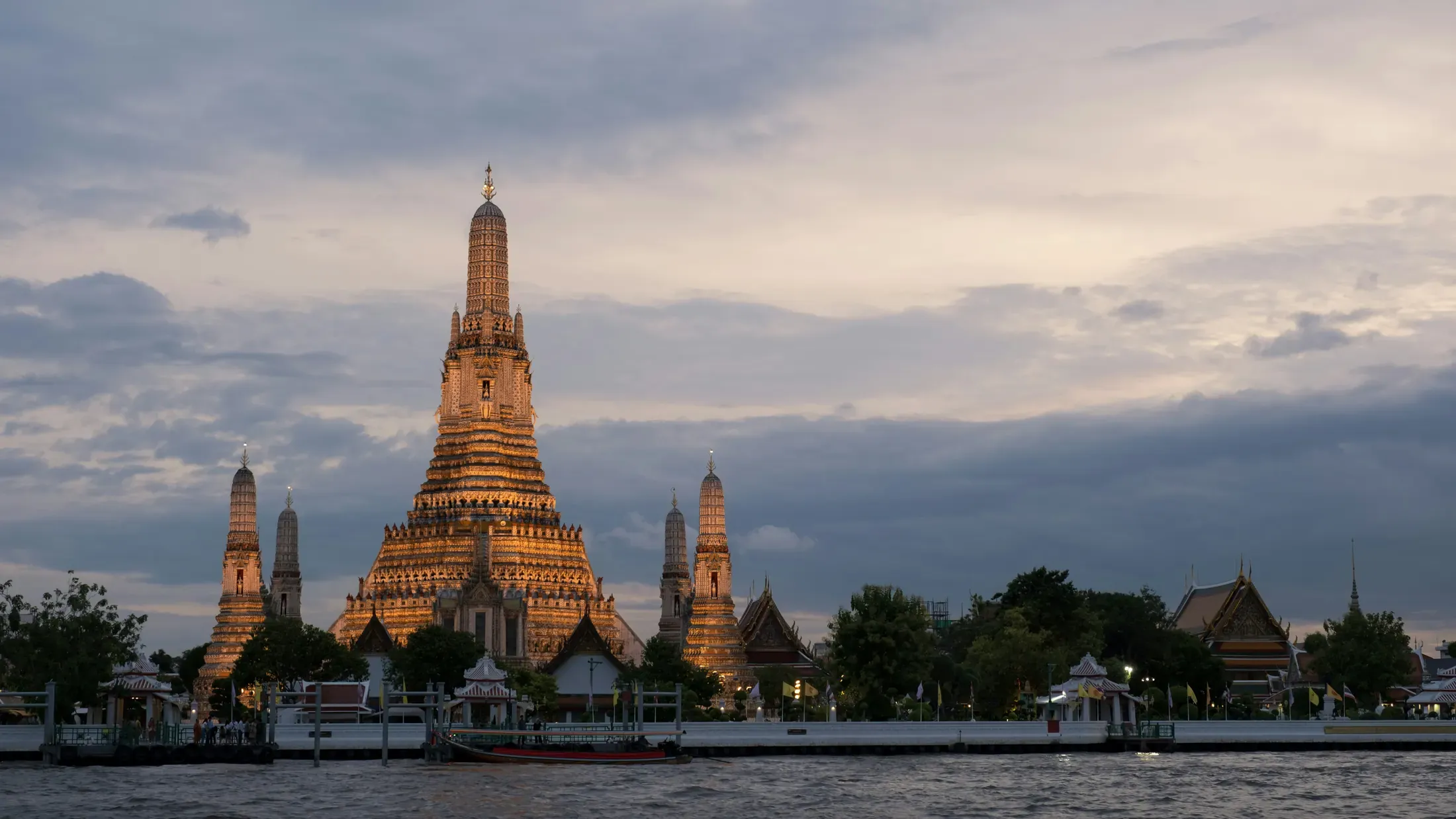 Three travelers walk beside the Chao Phraya River with Wat Arun in the distance.