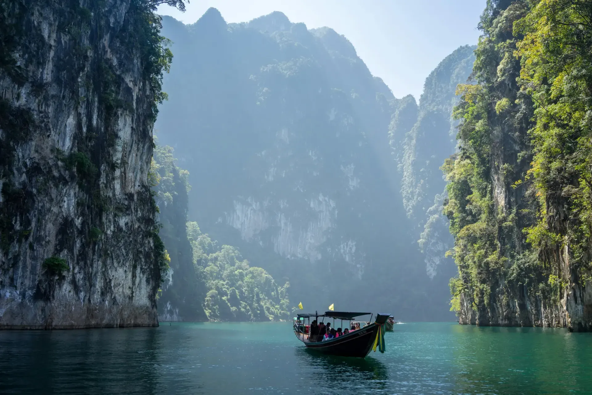 A longtail boat sails near Phuket limestone islands with a quiet beach in the distance.