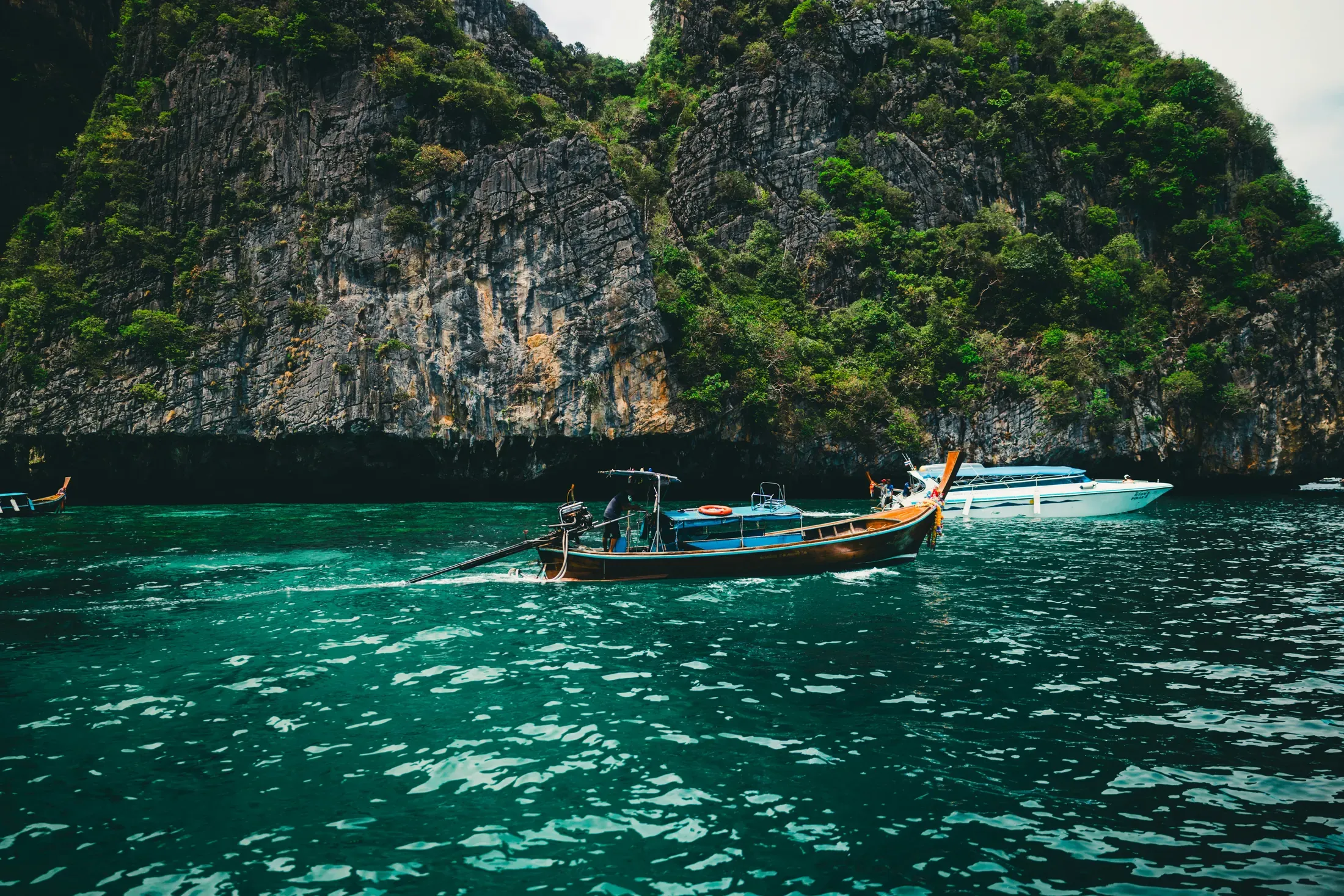A couple overlooks the sea from a Phuket resort terrace with palms and a distant boat.
