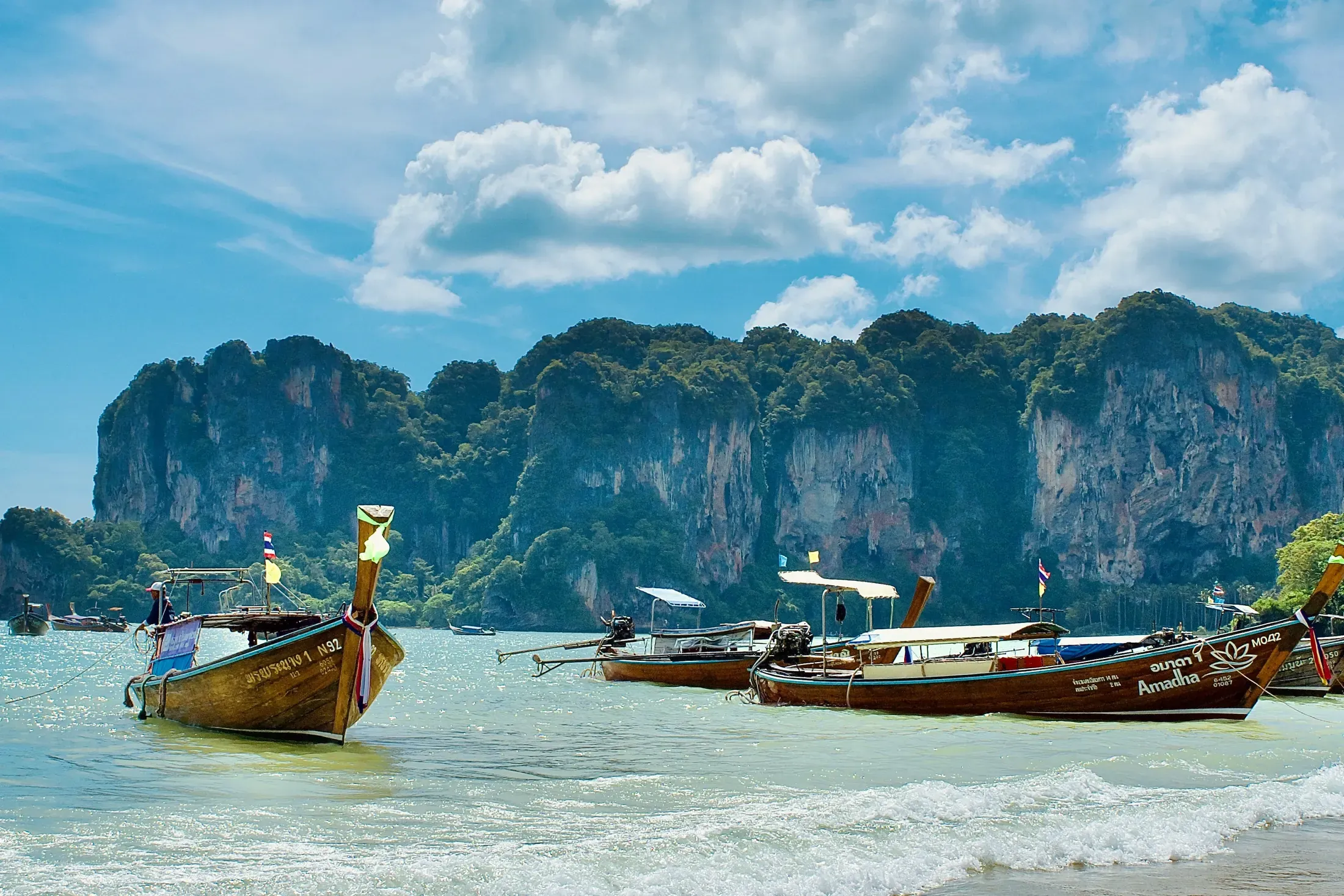 Quiet Thai beach with palms, turquoise water, pale sand, and a distant longtail boat.